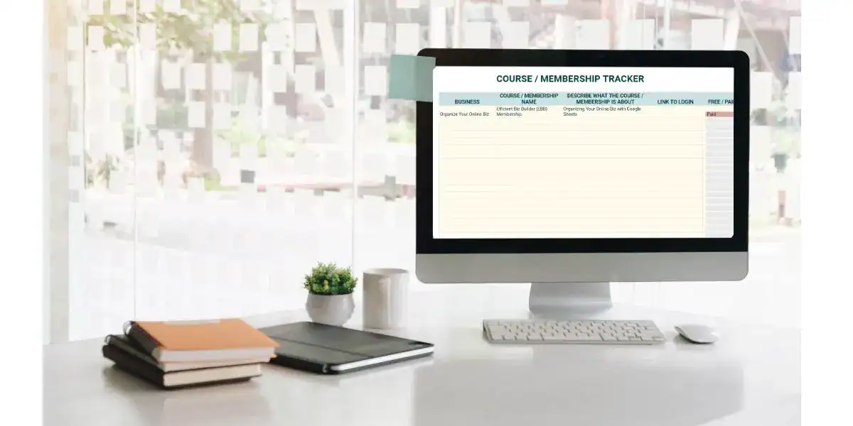 Desktop computer displaying a “Course / Membership Tracker” spreadsheet in Google Sheets, listing a course under “Organize Your Online Biz” with columns for name, description, login link, and whether it’s free or paid. The clean desk setup includes a stack of notebooks, a tablet, a small plant, and a mug by a bright window.